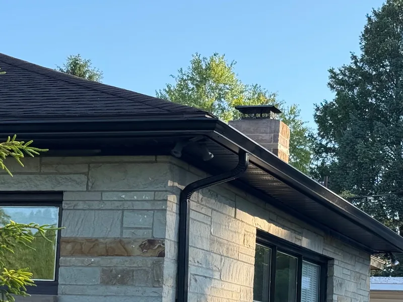 Black steel soffit and black seamless gutters along the roofline of a stone-sided exterior
