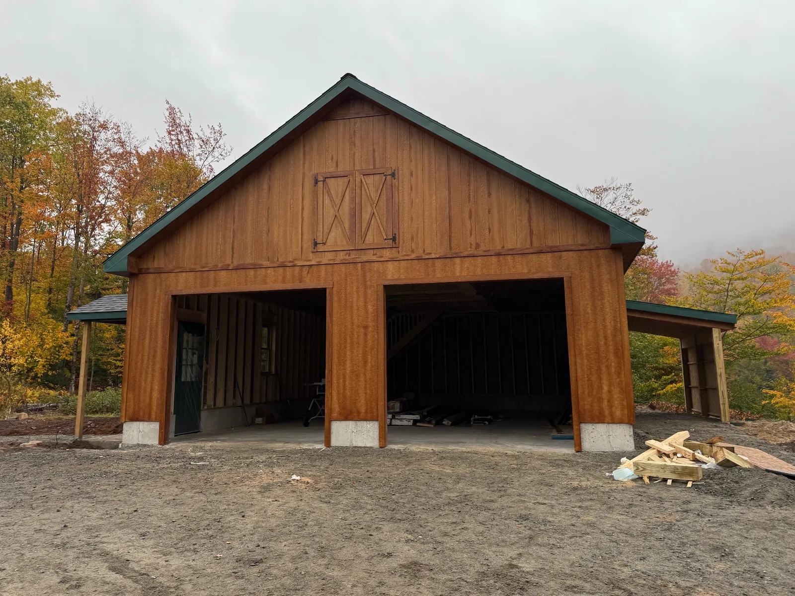 Wood-sided garage with two open vehicle bays and custom wooden double doors on the second floor