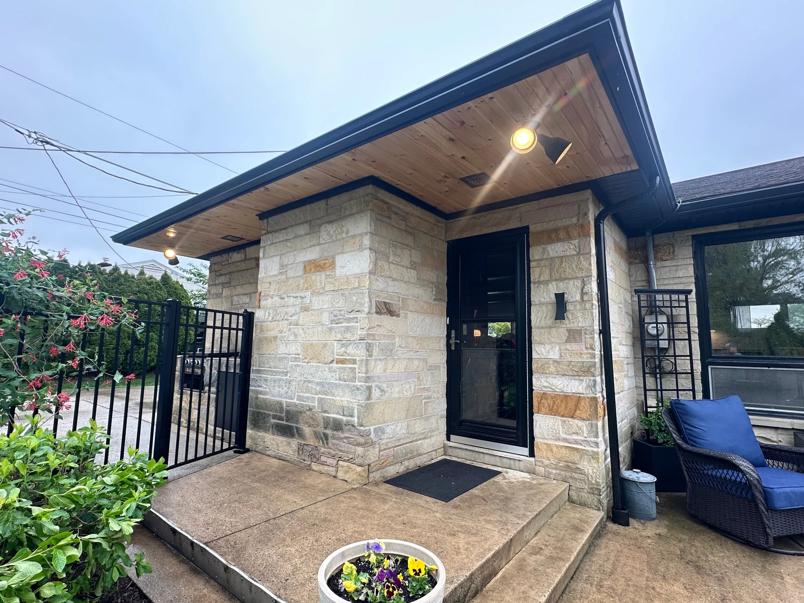 Sealed pine exterior ceiling above a stone entry, with a black aluminum gutter and black steel soffit